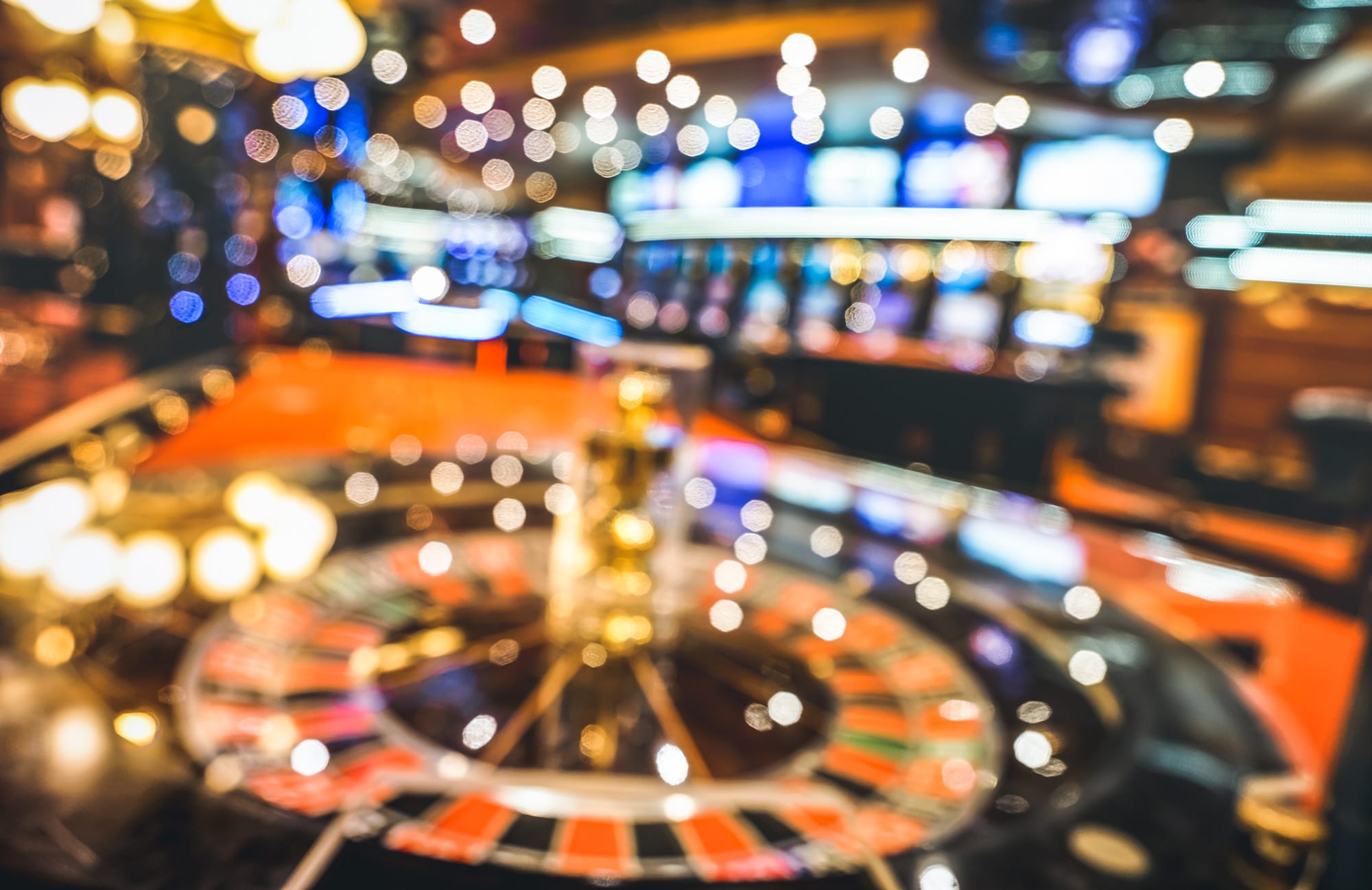 Softly blurred casino interior with a roulette wheel in the foreground.